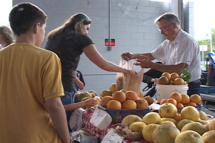 people are buying fruit at a vendor table