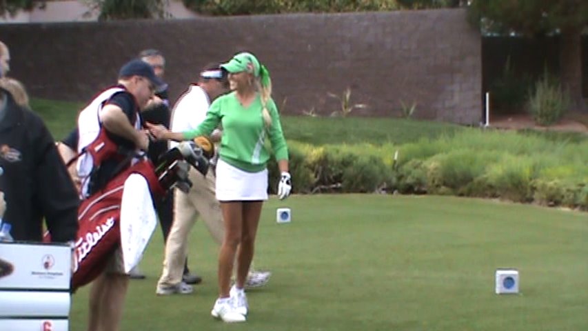 a woman in green and white golf attire holding her golf clubs