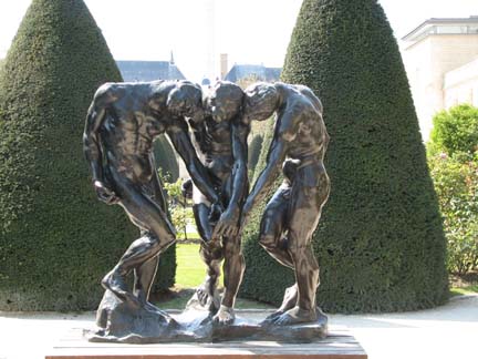 two silver statues are touching each other near some shrubs