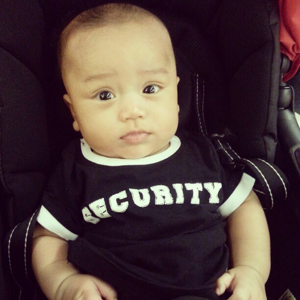 a young baby wearing a security shirt sits in a stroller