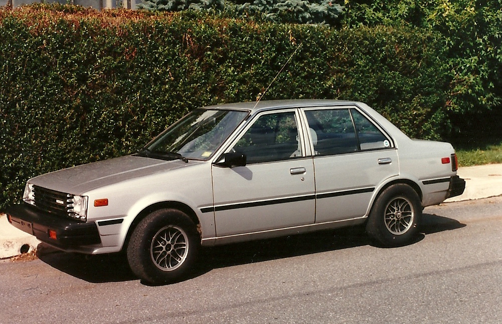 a silver car is parked in front of the hedge