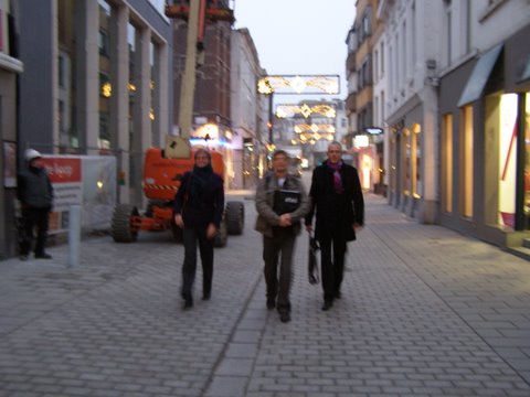 three people walking in front of stores on the sidewalk