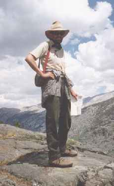 a person in cowboy gear stands on a rocky cliff