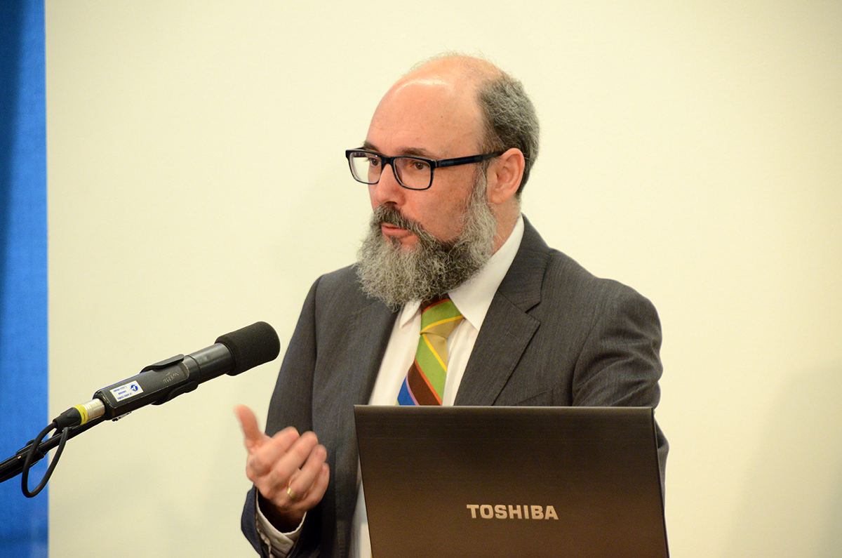 a bearded businessman at a podium holding a laptop