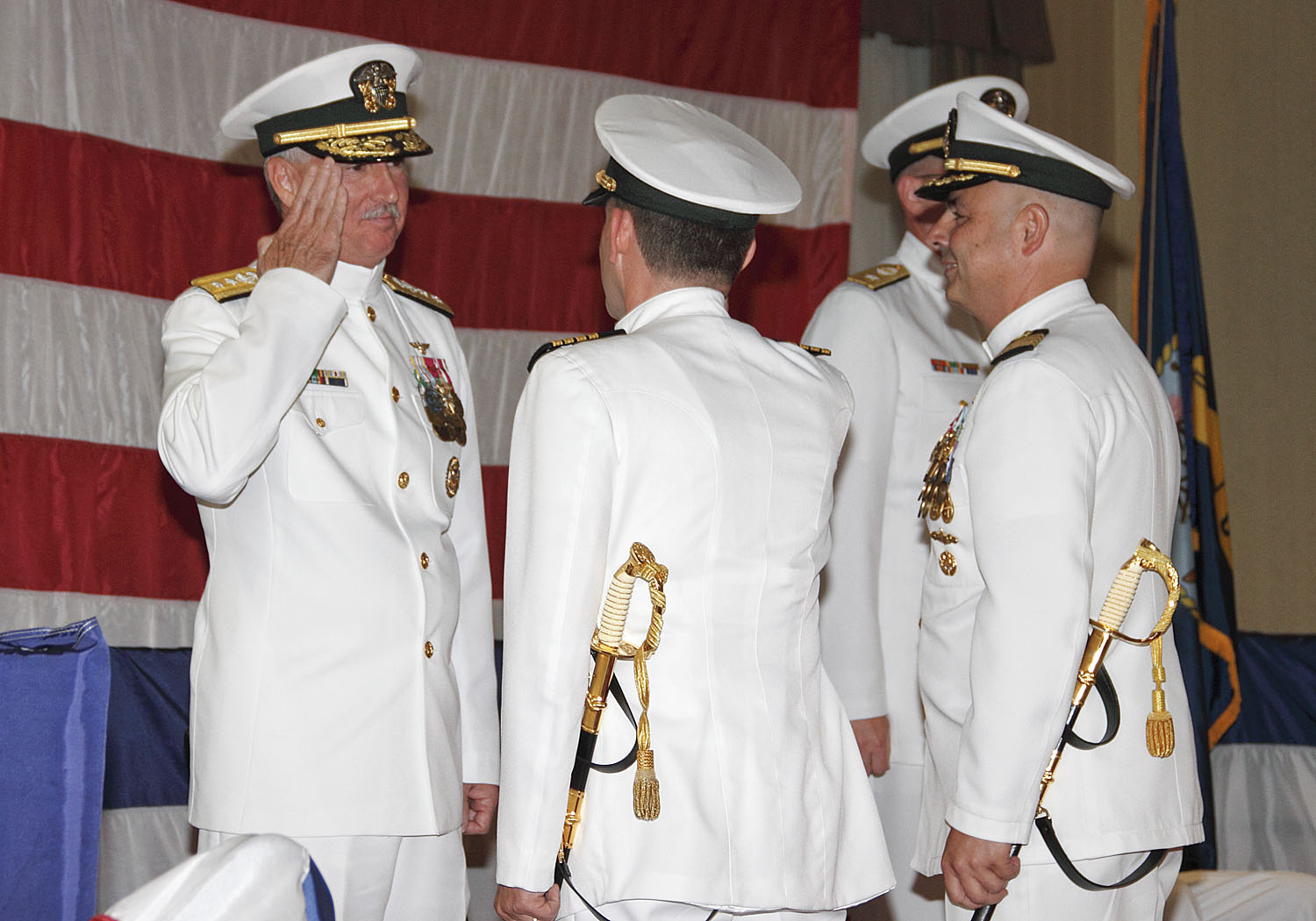 four military men in white uniforms standing next to a flag