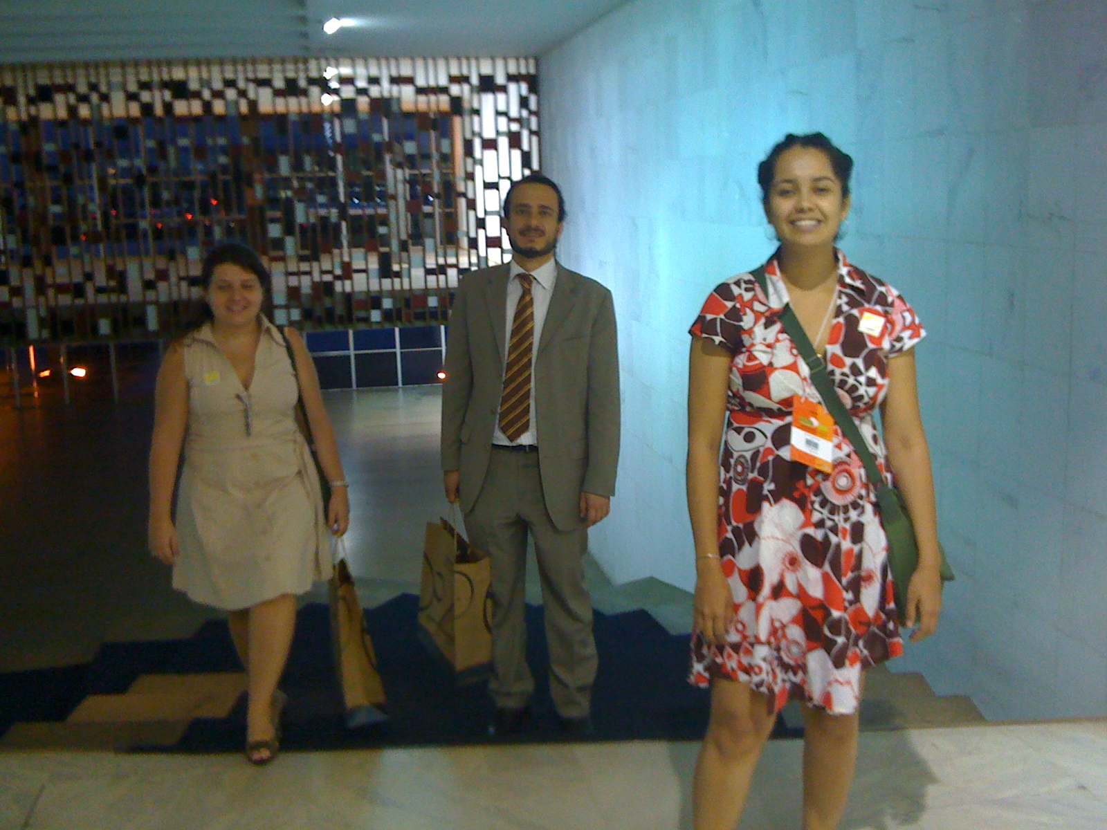 three people wearing clothing and standing in an office hallway