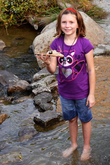 girl in purple shirt holding small brown stick standing in river