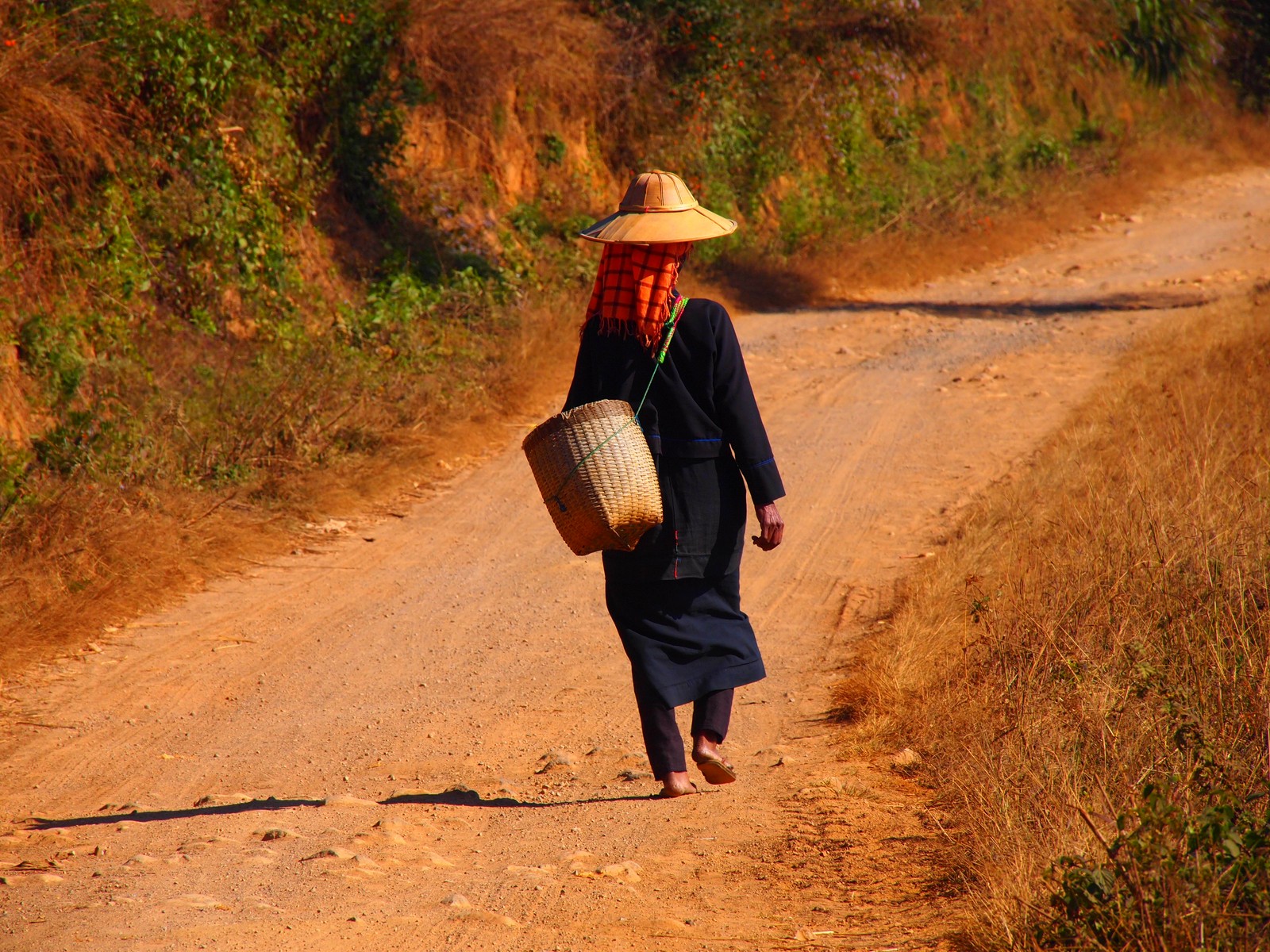 a person wearing a hat walking down a dirt road