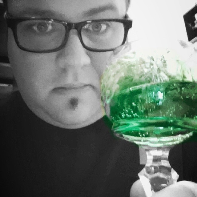 a man is drinking some green liquid in a wine glass