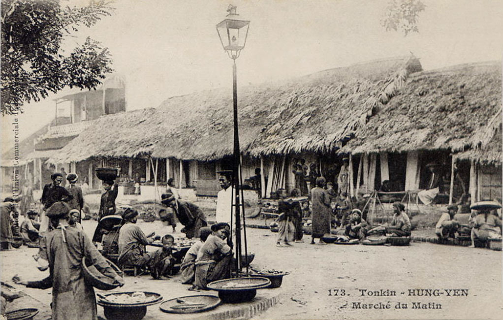 old black and white pograph of people sitting outside a hut