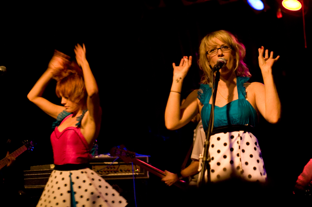 two girls on stage performing with arms in the air