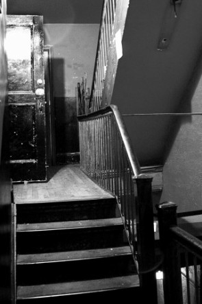 a wooden stairway and metal handrail next to an overhanging stairwell