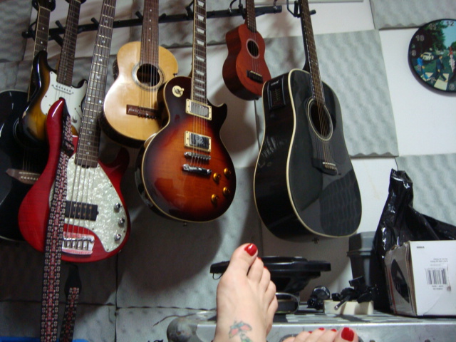 a person's foot on the floor in front of a rack of guitars