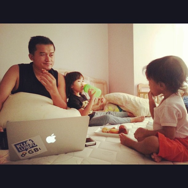 a man and two children sit on the bed in front of an apple laptop