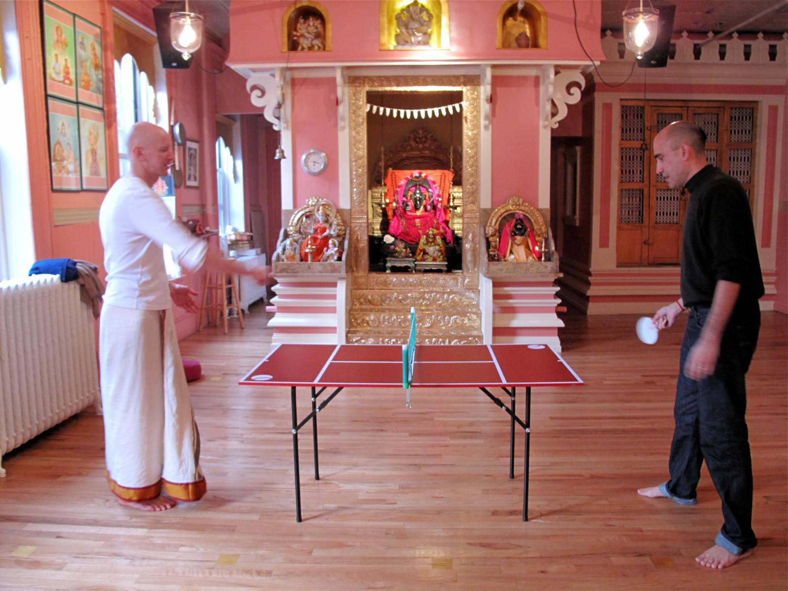two men are playing table tennis in a pink room