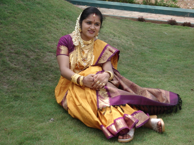 indian woman wearing an orange and purple outfit and jewelry on grass