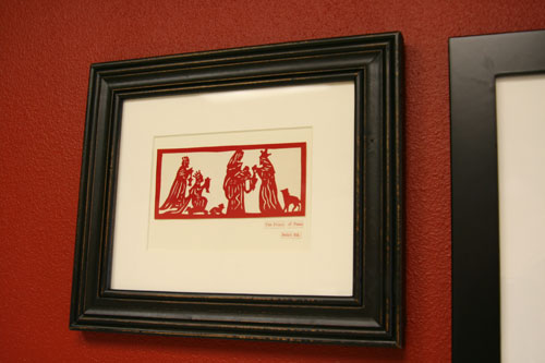 the framed painting of the red and black artwork is on a red wall