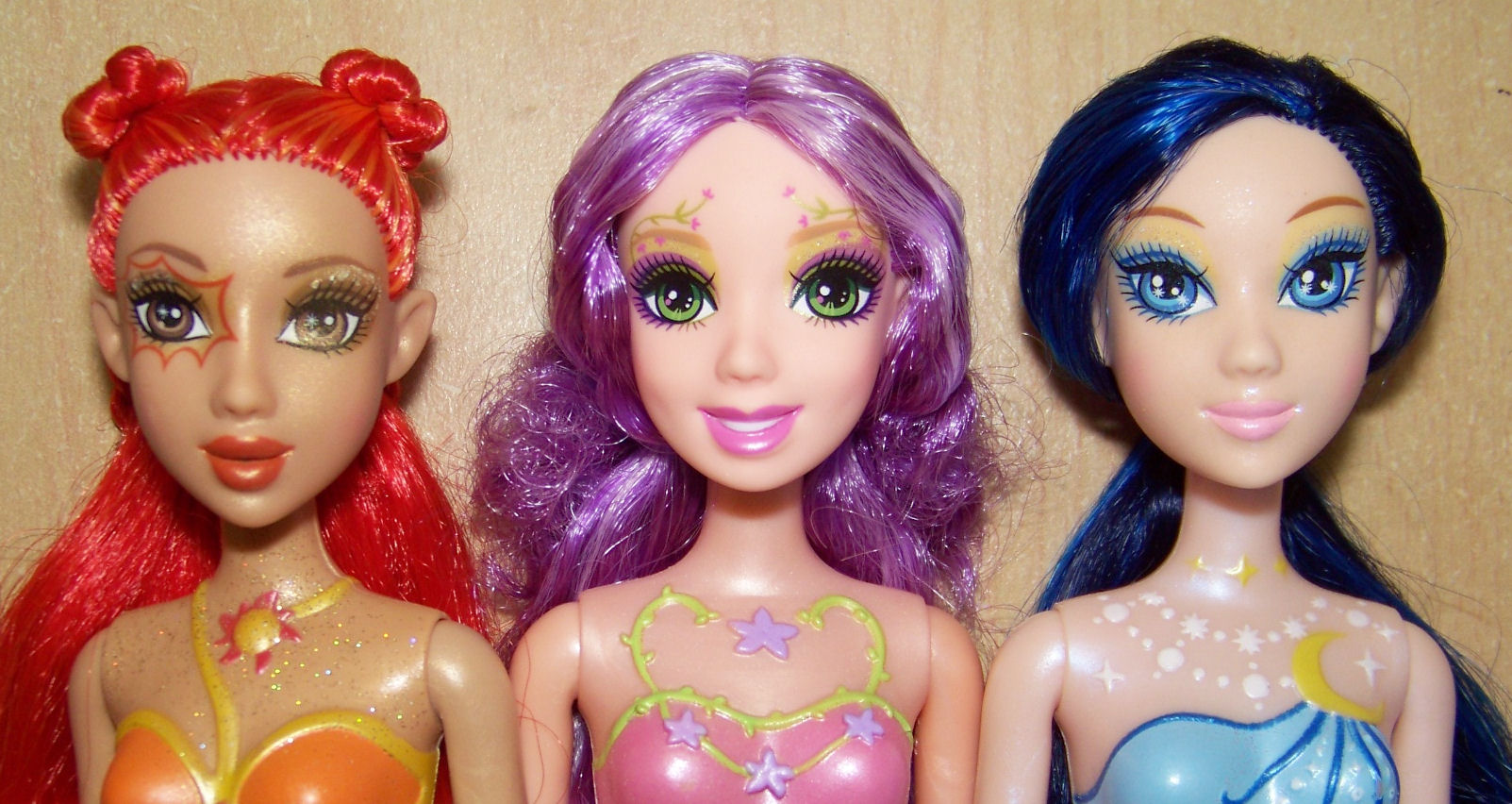 three dolls wearing costumes, including one with pink and orange hair