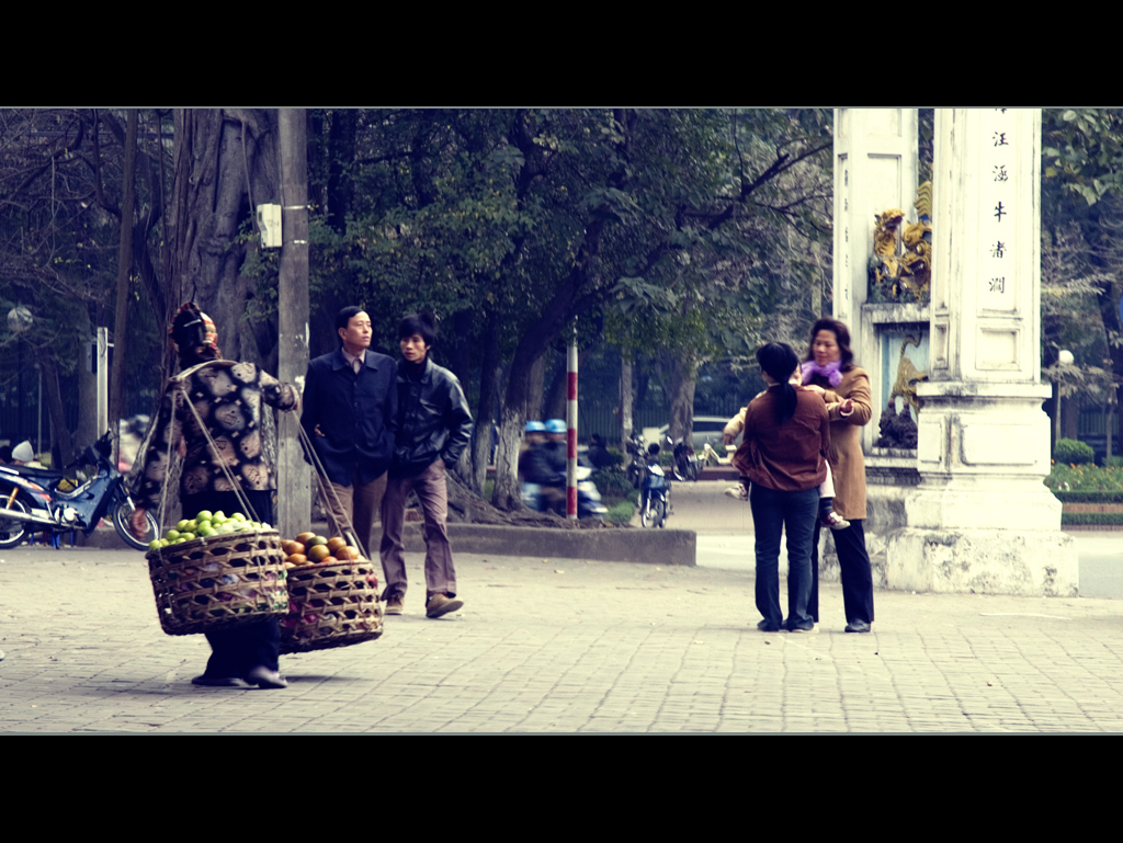 several people on a bricked sidewalk carrying baskets and fruit