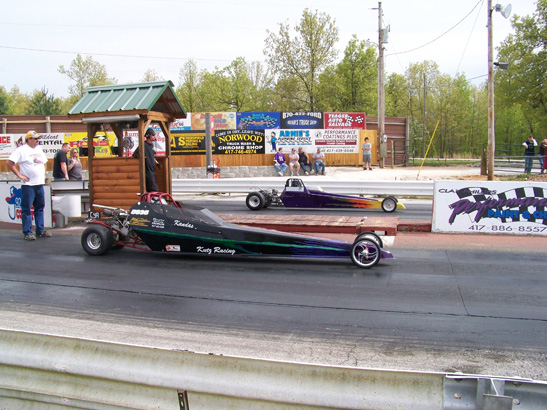 a drag car at a drag track and a man standing by