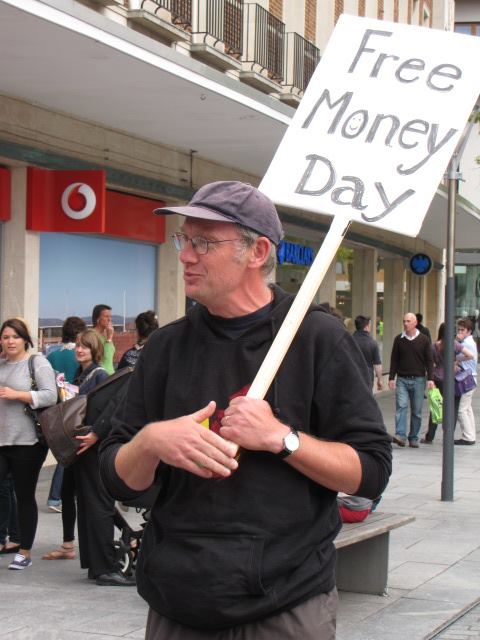 a man is standing on a sidewalk holding a free money day sign