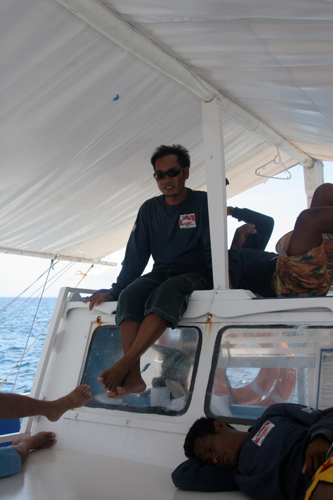 two men sitting in a boat while another man sits on the floor