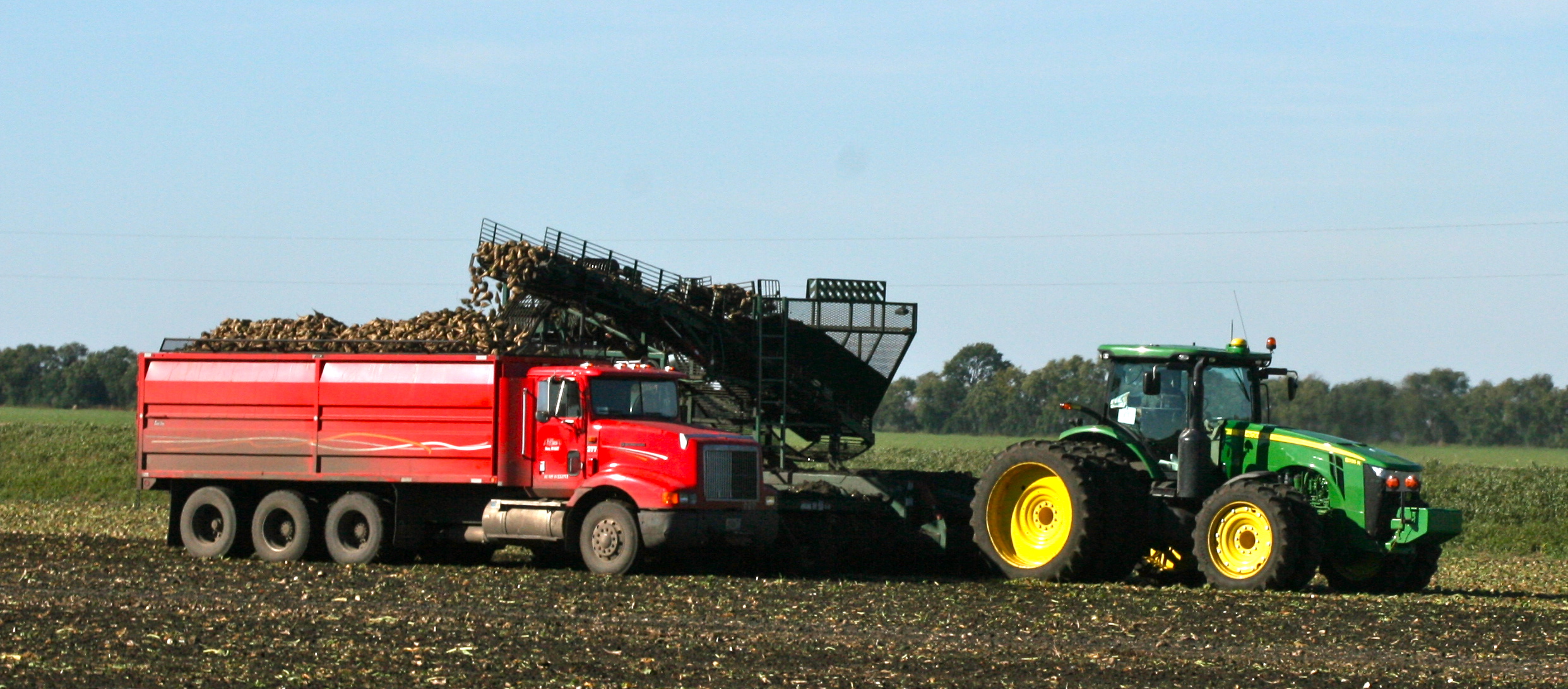 two tractors are driving on a farm near a large tractor