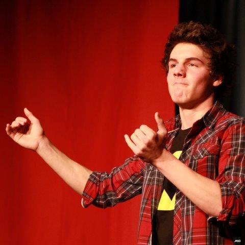 young man wearing plaid shirt gestures to an audience