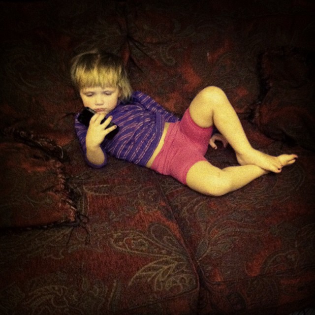 a toddler on her cell phone lying on a bed