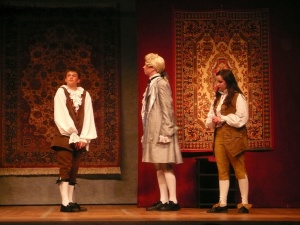 four performers dressed as a merchant and maid stand in an old world setting