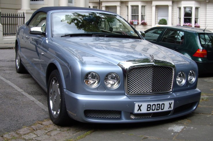 silver bentley with chrome lettering parked in front of some buildings