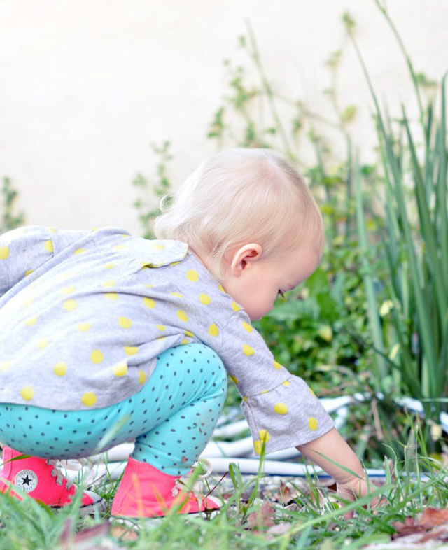 a little baby kneeling down with a toy in the grass