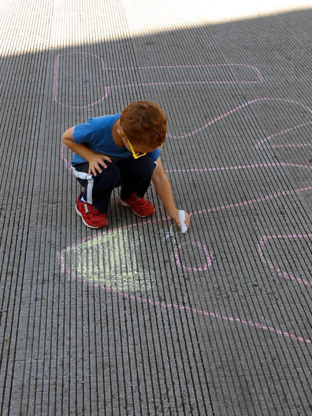 a little boy crouching down to draw some type of chalk