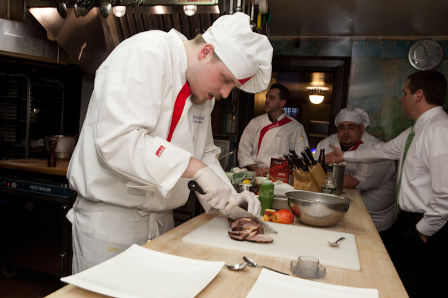 a man with chef attire and goggles in a kitchen slicing meat