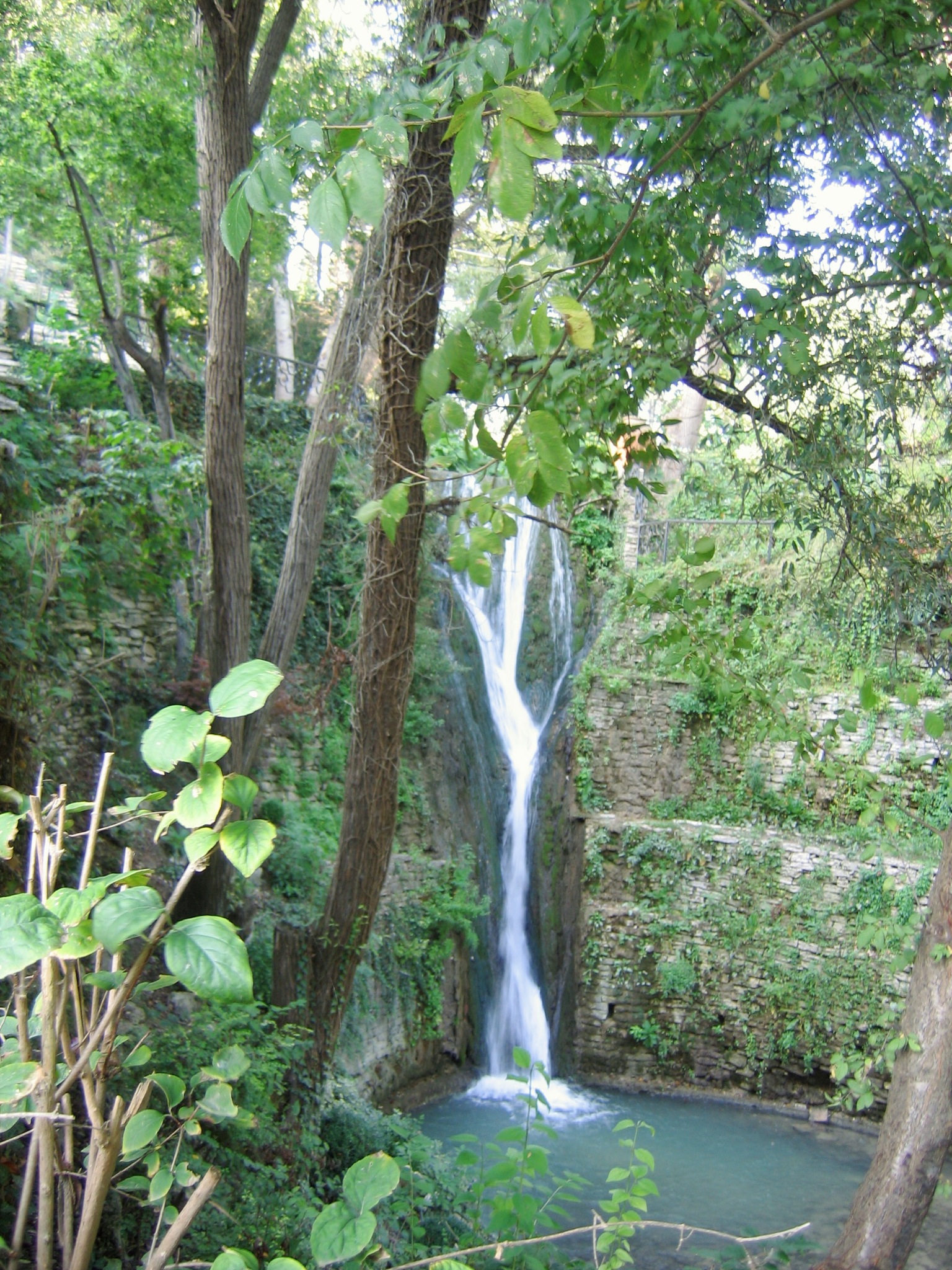 a tall waterfall next to several trees with a body of water running down it