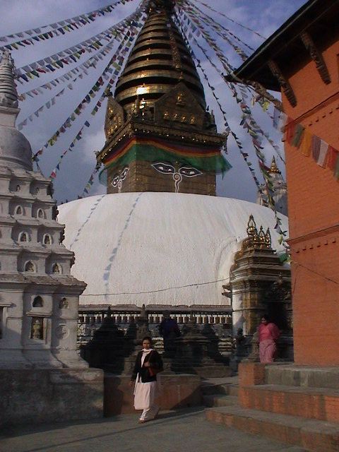 woman wearing traditional dress, standing at the base of large stuyr stu with many buddhist flags flying around
