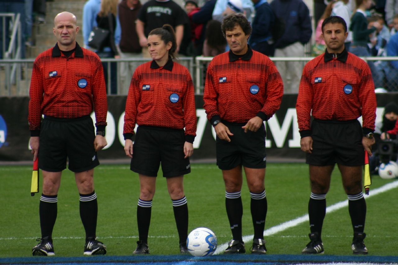 three soccer players dressed in uniforms stand together near a soccer ball