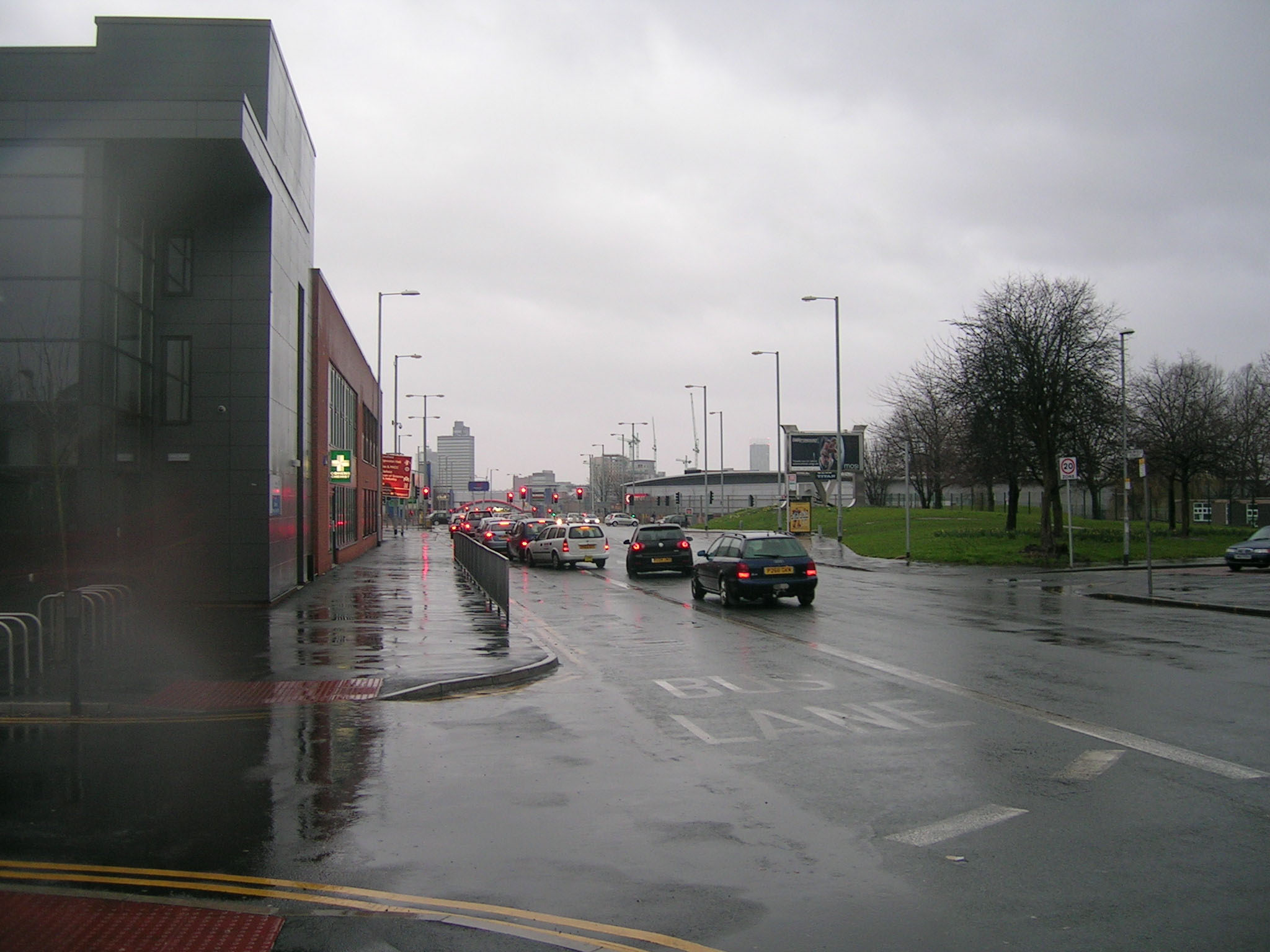 a busy street in the rain and cars parked on the side walk