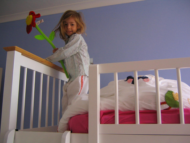 a girl stands on her bed as she plays with a doll