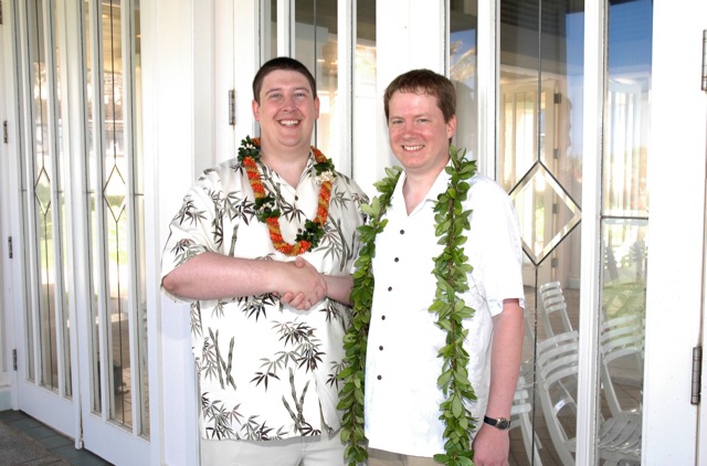 two men pose with one another wearing a lei