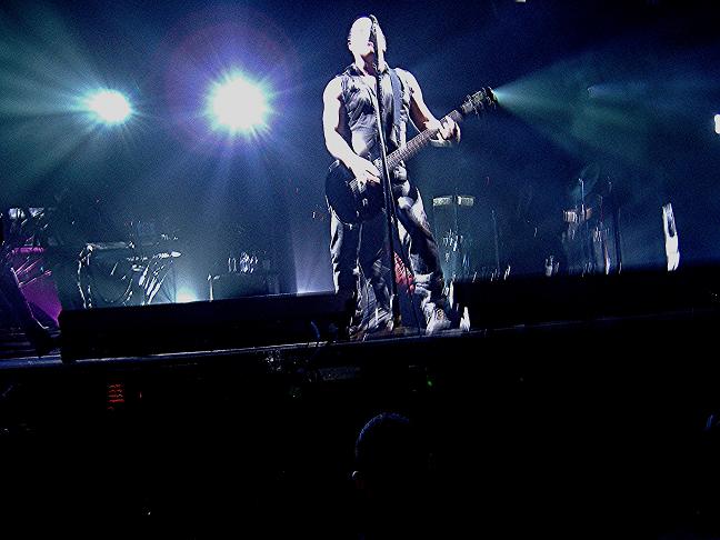 some people in concert with purple lighting and two guitarists