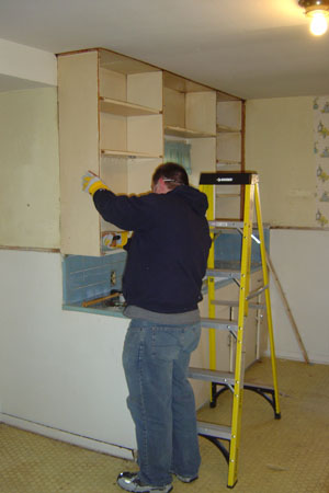 man fixing cabinets in unfinished house with yellow ladder