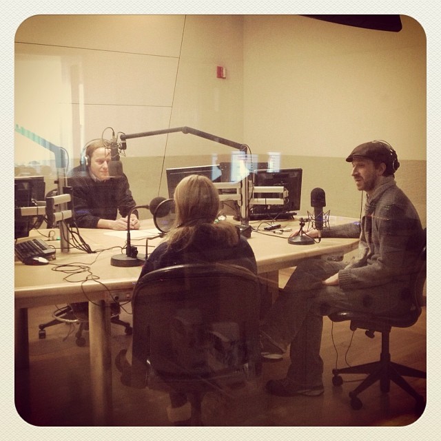 three people sitting around a large table talking to a radio announcer