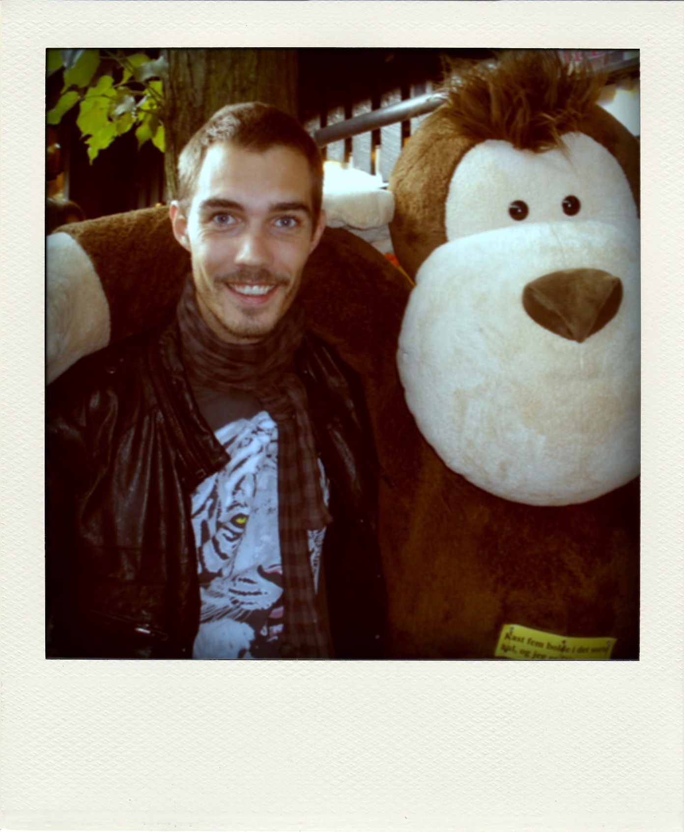 man wearing a jacket and scarf with a huge teddy bear behind him