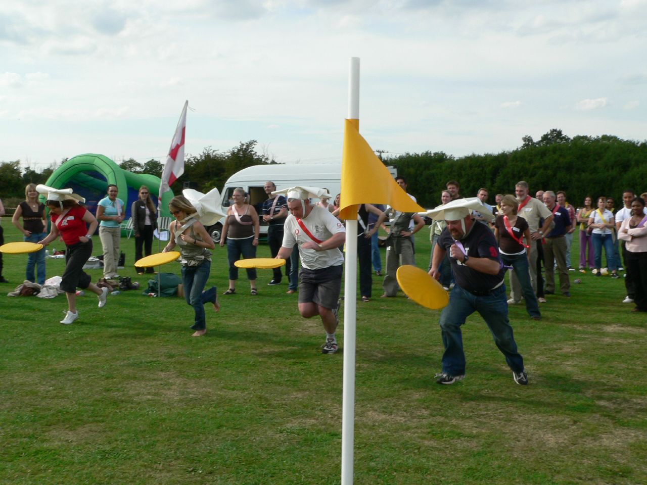 a crowd of people playing games on grass with frisbees