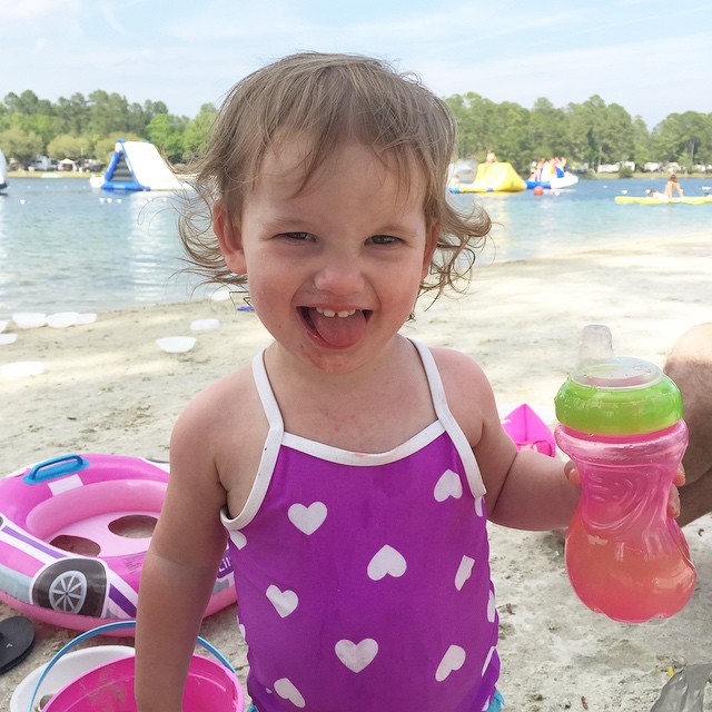 a little girl drinking a bottle next to a lake