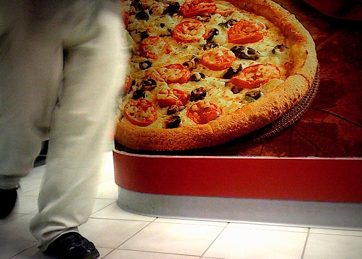 a person standing next to a large pizza