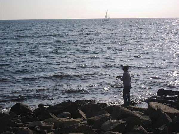 man standing on rocky shoreline with large body of water in the background