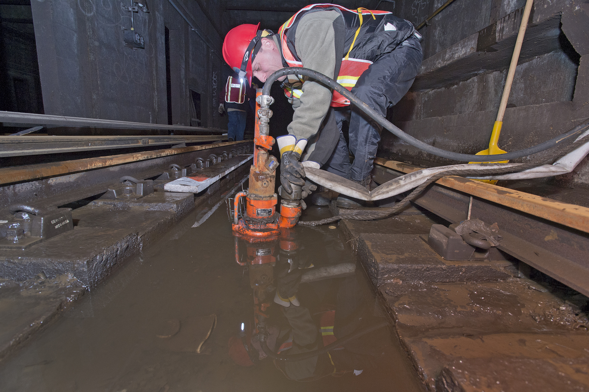 a construction worker wearing hardhats, safety helmet and holding a hose to a drain