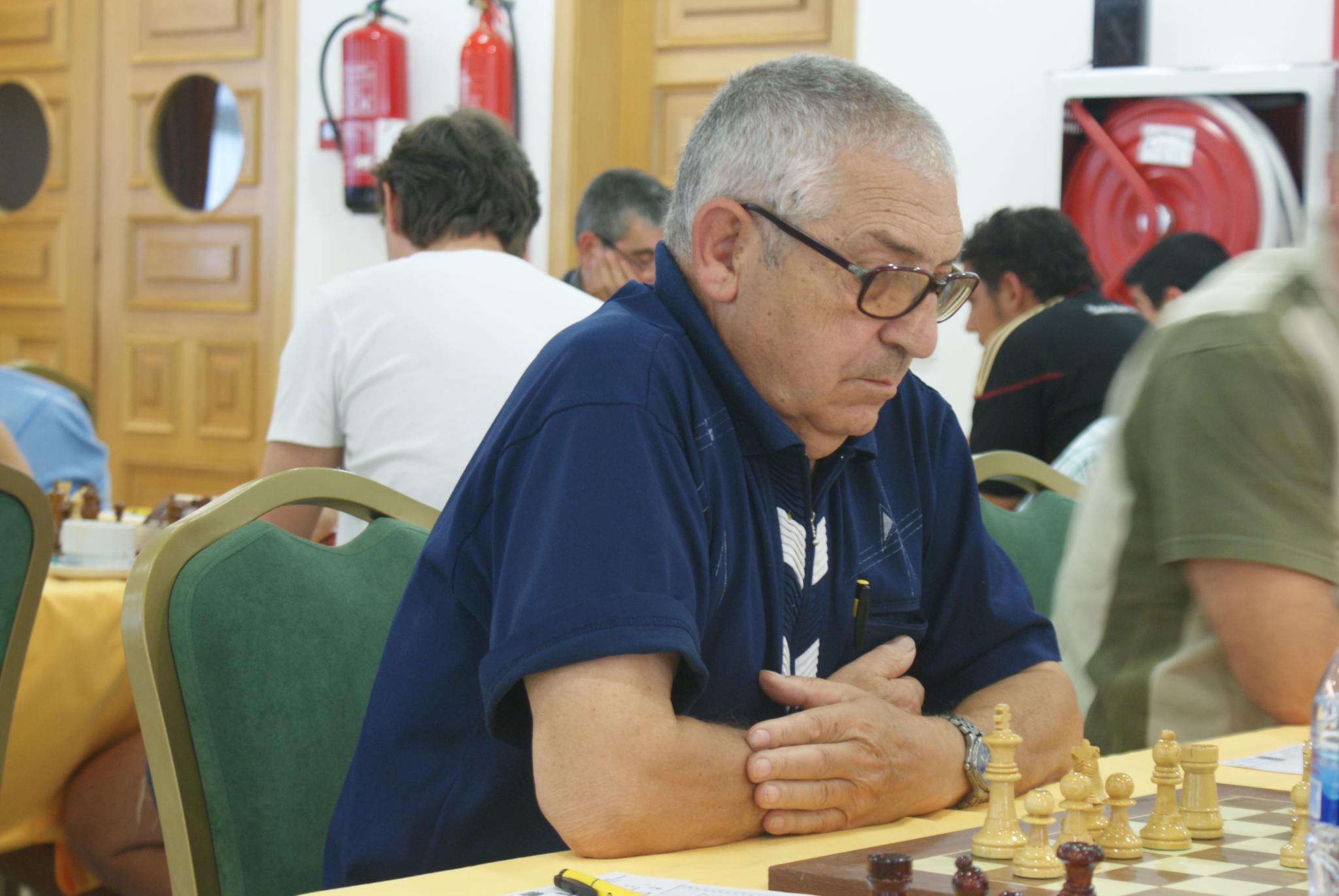 a man playing chess in a room with people sitting around
